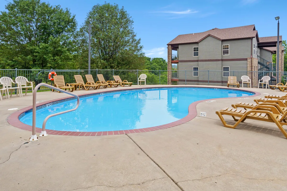 A sparkling swimming pool surrounded by lounge chairs and lush greenery offers a glimpse of the resort's amenities. The inviting outdoor setting hints at leisurely afternoons spent swimming, sunbathing, or socializing after exploring Branson's attractions.