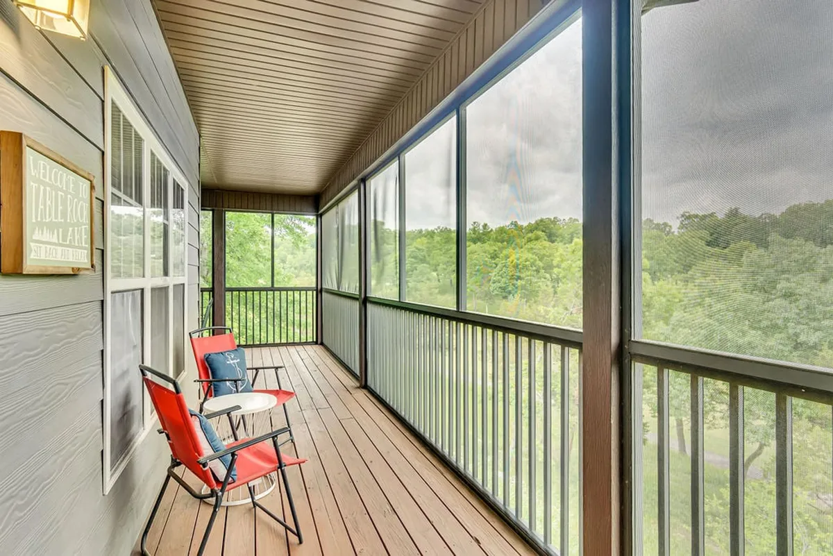 A charming screened-in porch featuring two red chairs and a small white table, with lush greenery visible through the mesh screens. The setting is tranquil, designed for relaxation and enjoying the outdoors without the inconvenience of bugs. The view beyond the porch hints at open fairway or natural landscapes, inviting the outside in.