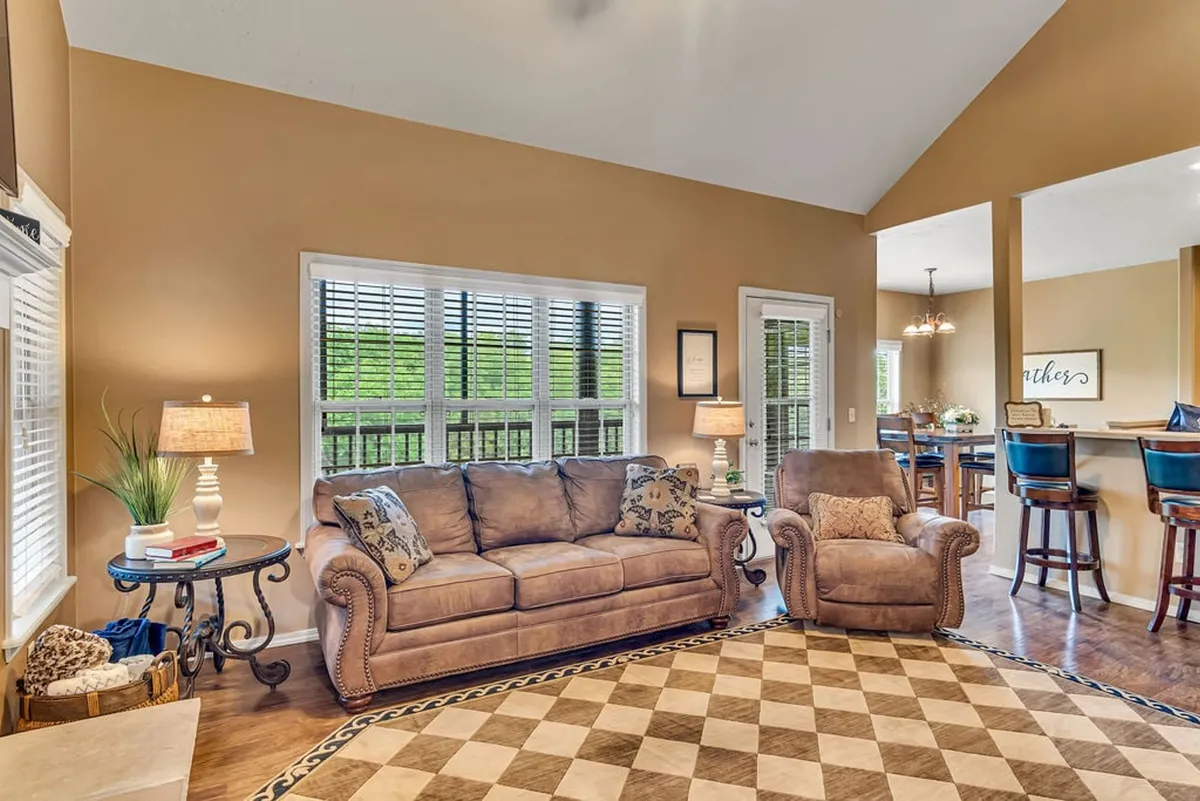 A comfortable living room with a soft sofa, armchair, coffee table, and sunlit windows. The relaxed, welcoming atmosphere invites family and friends to gather and unwind.