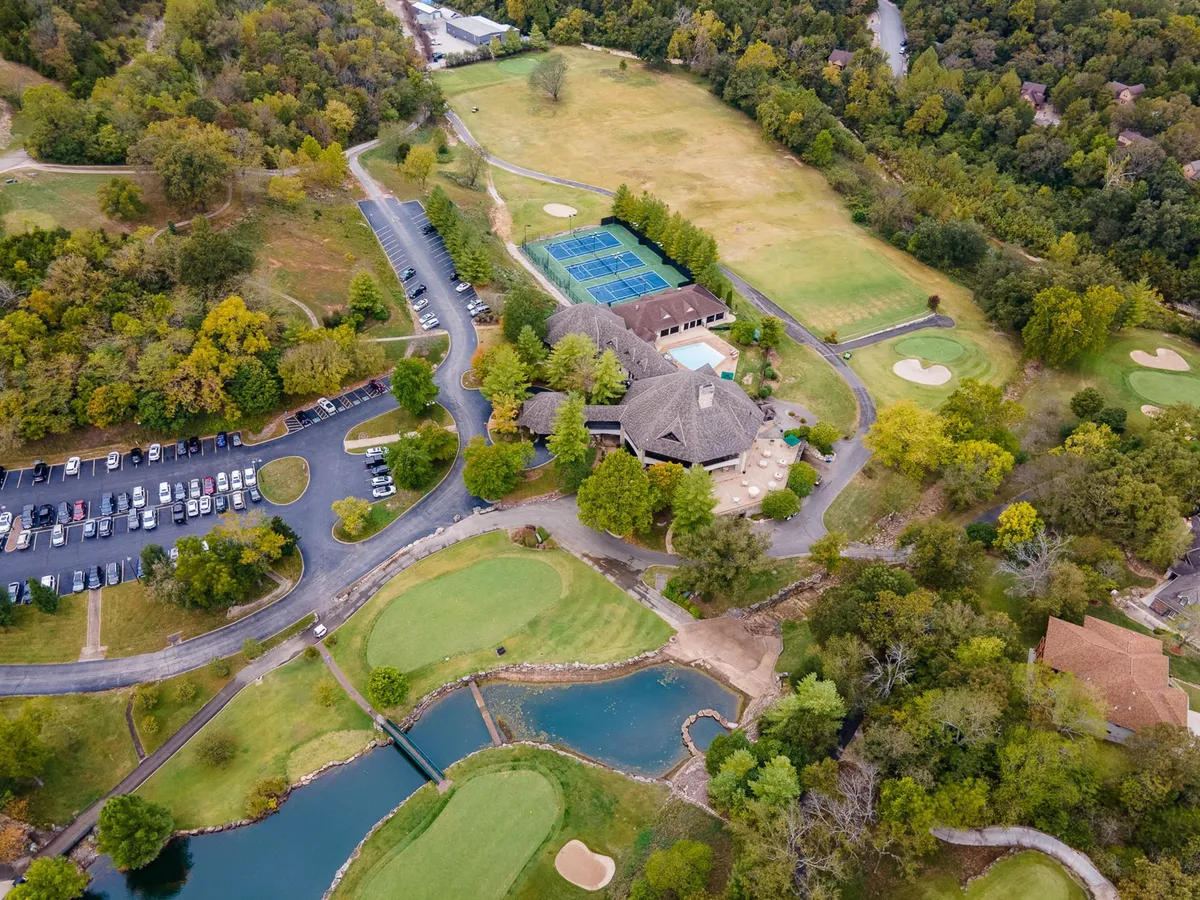 A wide aerial view capturing the resort's central amenities: the golf course, an inviting swimming pool, tennis courts, a parking area, and the clubhouse. The image conveys the integrated nature of the resort's recreational offerings, nestled amid greenery.
